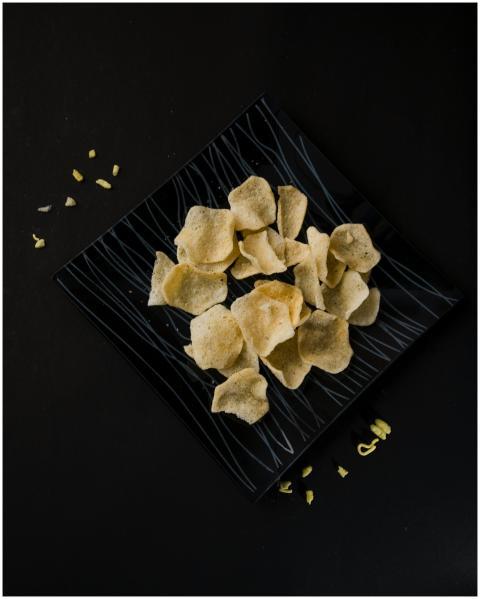 Black plate of crispy potato chips with small scat
