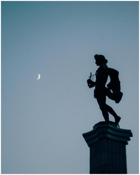 A silhouette of a statue stands against a serene b