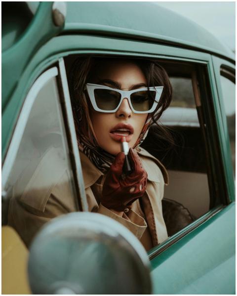 Stylish woman wearing sunglasses and applying lips