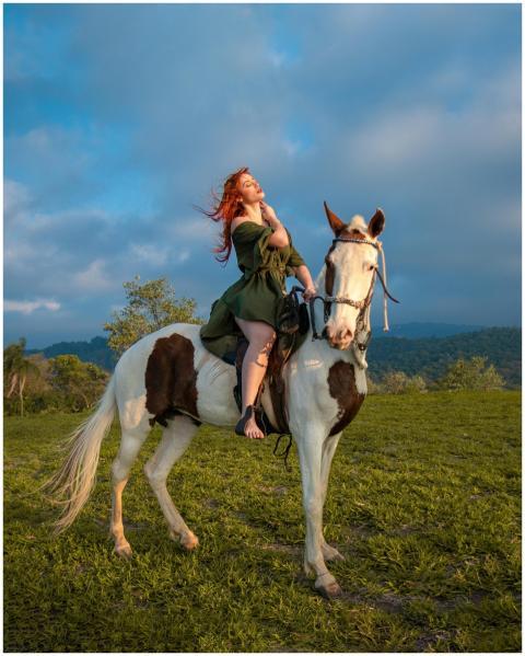 Red-haired woman riding a piebald horse in a lush