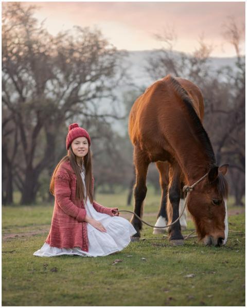 A young girl in a red knit outfit sits beside a gr