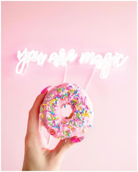 Vibrant donut with sprinkles held against a pink b