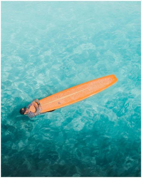 Surfer relaxing on an orange surfboard in clear bl