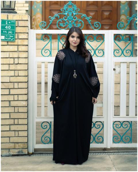 Woman in a black traditional outfit posing by a de