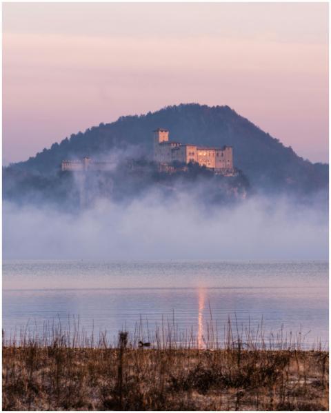 Majestic castle atop a misty hill by Lake Maggiore