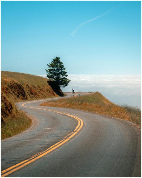 Winding mountain road above clouds with lone cycli