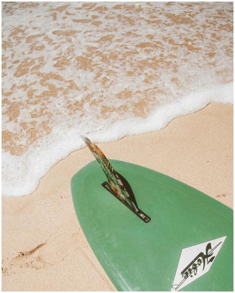 A green surfboard rests on the sandy beach with oc