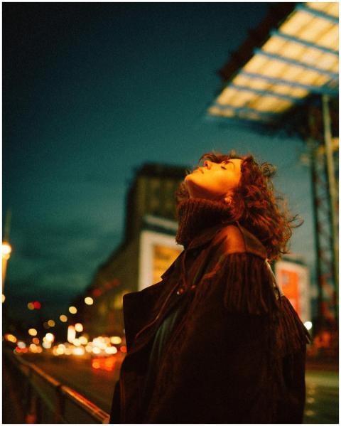 A woman in a coat looks up on vibrant city street