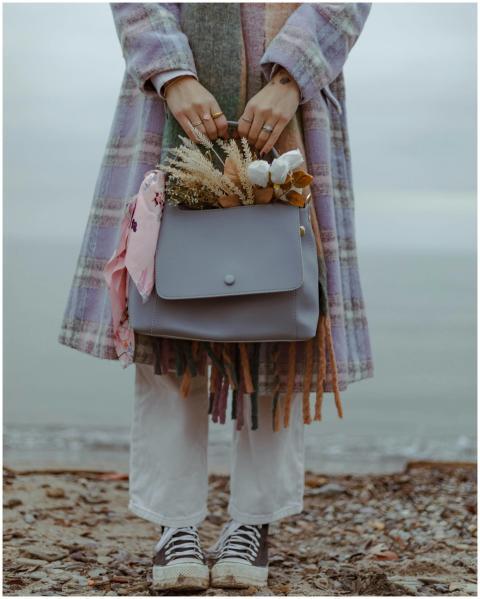 A woman in a coat holds a handbag with flowers, st