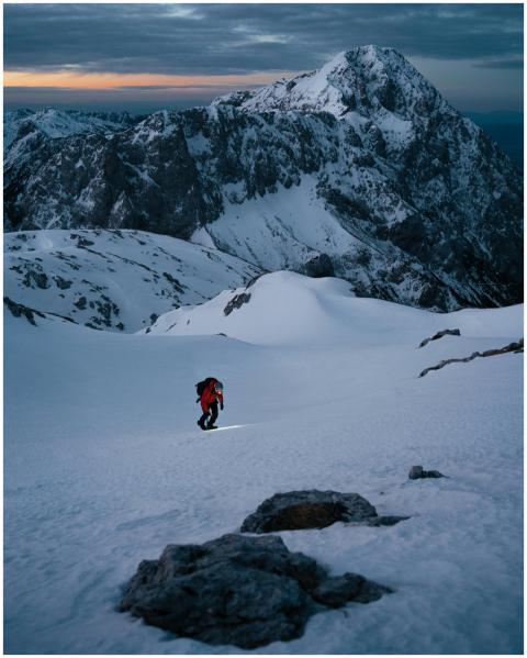 Lone mountaineer trekking up a snow-covered peak a