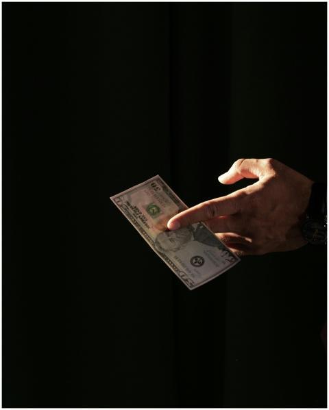 A close-up of a hand holding a US dollar bill agai