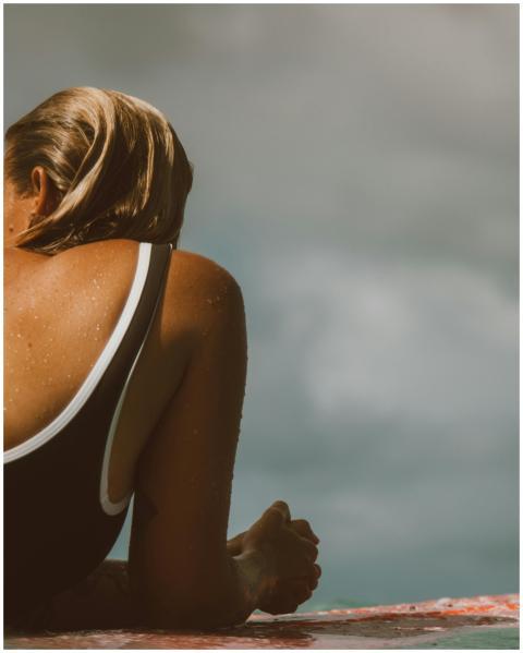 A woman lying on a surfboard in a bathing suit, en