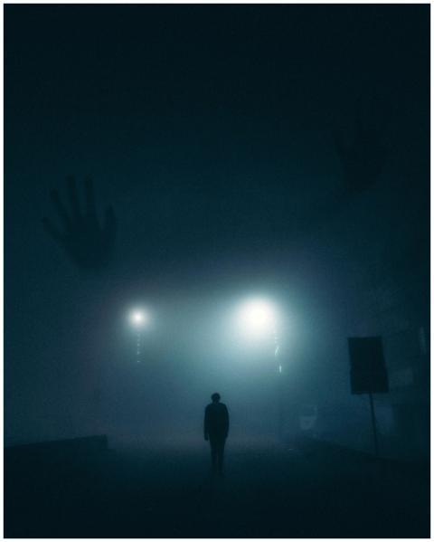 A lone silhouette walks through a foggy street in