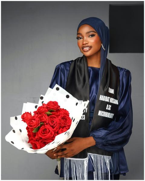 Young woman in graduation attire holding bouquet o
