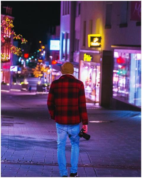 Photographer walking down a neon-lit city street c