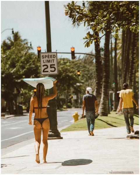 A woman in swimwear carries a surfboard on a sunny