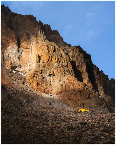 A vibrant yellow tent sits at the base of a rocky