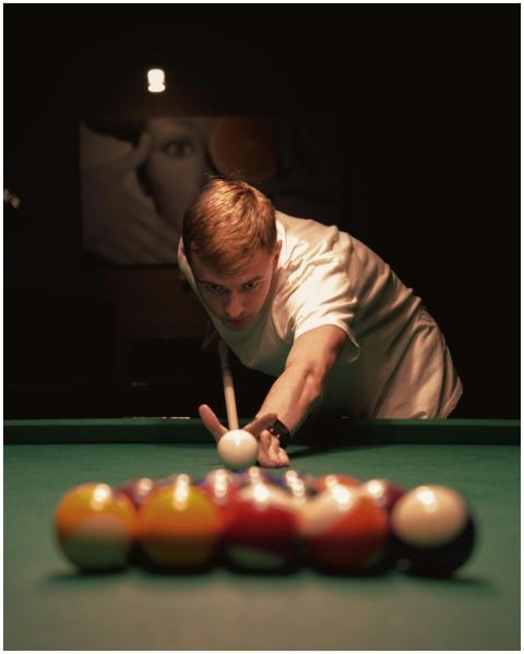 A young man intensely focuses on making a billiard