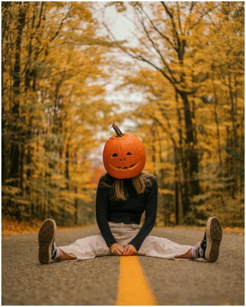 Person with pumpkin head sitting on forest road in