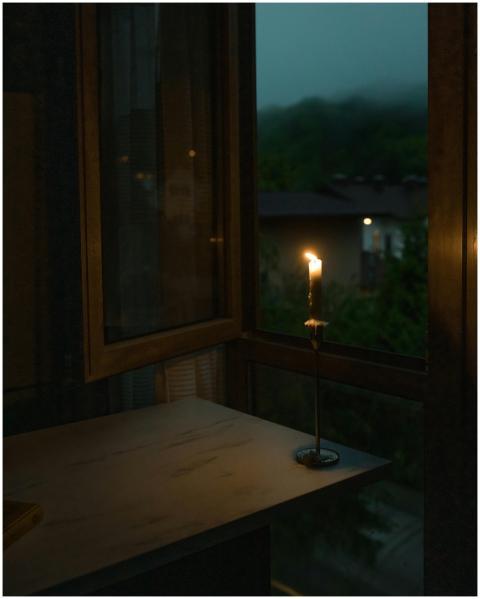 A warm candle flickers by a window, casting light