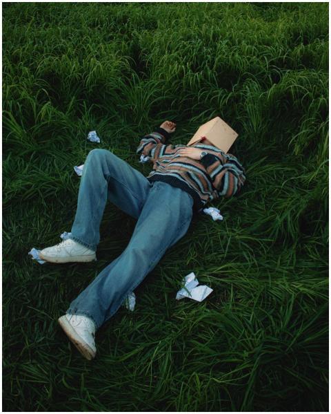 A person in casual attire lies on grass with a boo
