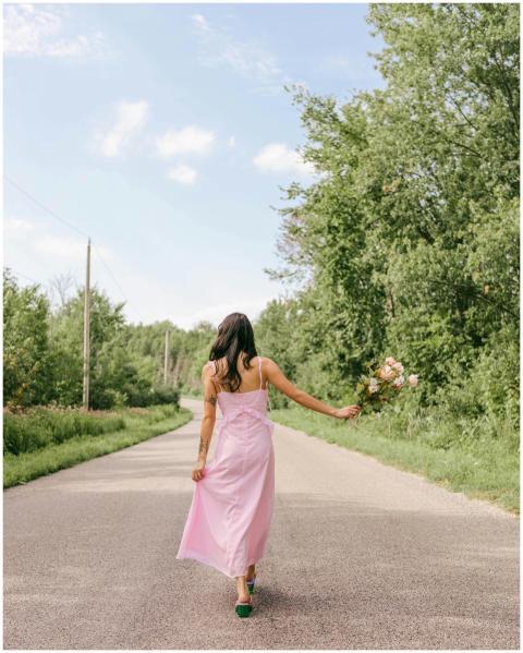 A woman in a pink dress walks on a countryside roa