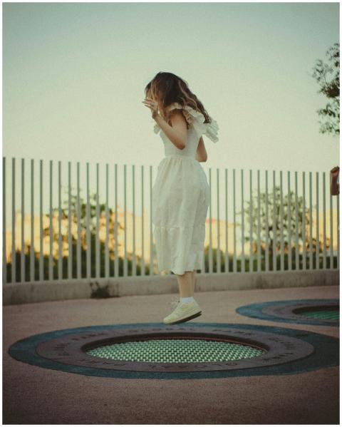A young woman in a white dress joyfully jumps on a