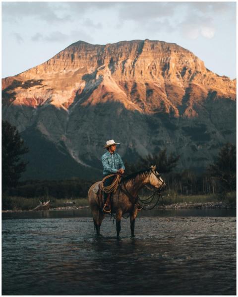A cowboy rides his horse across a scenic river in
