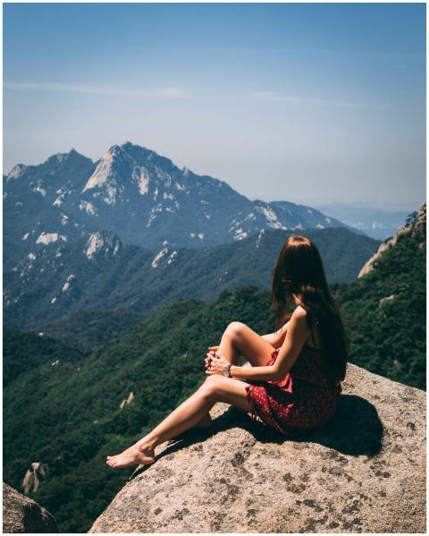 A woman sitting on a rock, admiring scenic mountai