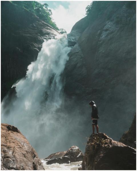 A man standing near a breathtaking waterfall in Ba
