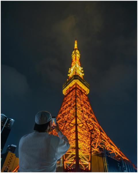 A person photographs the illuminated Tokyo Tower a