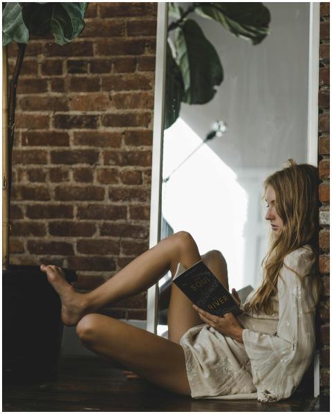 Serene woman reading by a mirror with brick wall b