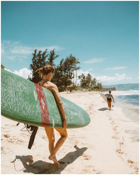 Two women walking on a sandy Hawaiian beach carryi