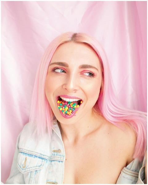 A woman with pink hair poses playfully with colorf