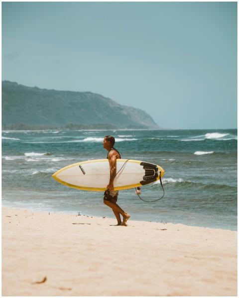 A man walking on sandy beach carrying a surfboard