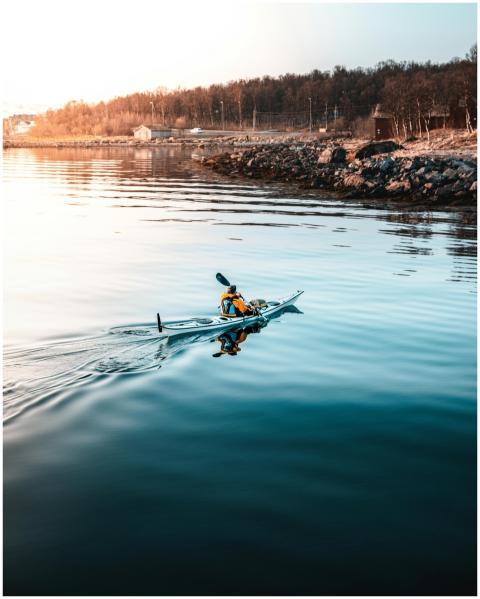 Kayaker paddles across calm waters near a rocky sh