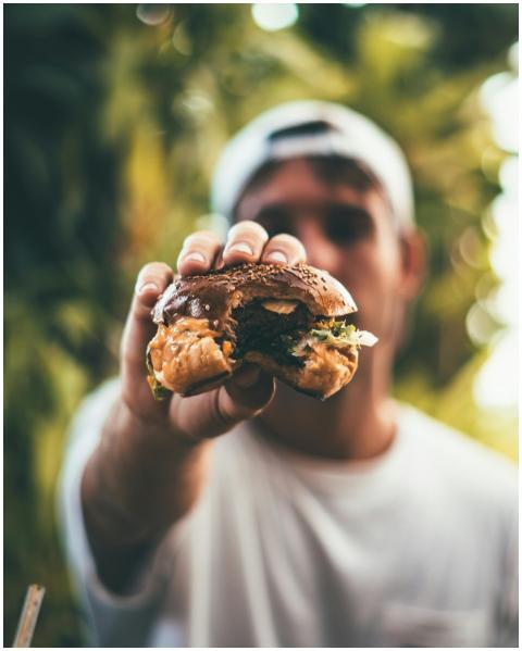 A man holds a juicy cheeseburger outdoors in dayli