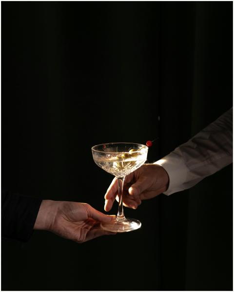 A close-up of two hands exchanging a martini cockt