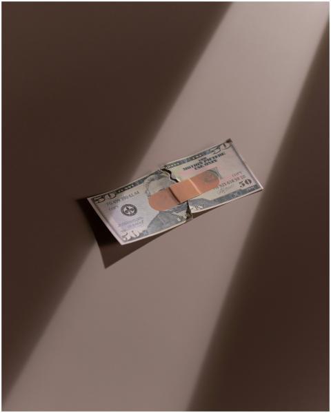 A torn dollar bill patched with a bandage, symboli