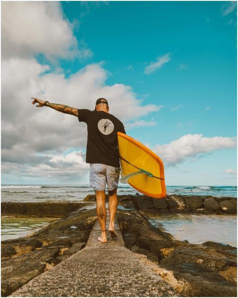 Man walking barefoot with surfboard on seaside pat
