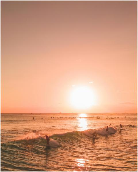 Surfers ride waves under a vibrant sunset sky, ref