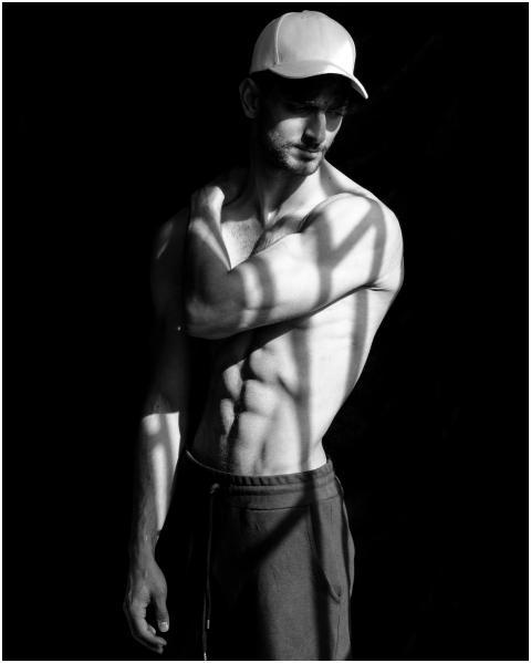 A muscular man posing shirtless with shadows and s