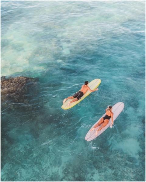 Two surfers paddle through turquoise waters, enjoy