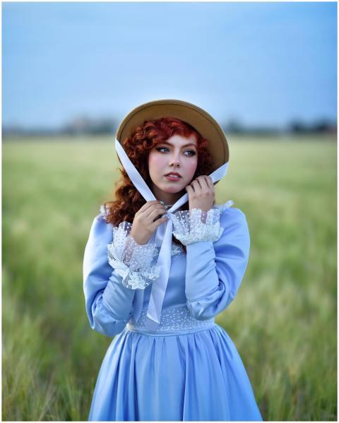 A woman in a blue vintage-style dress and bonnet s