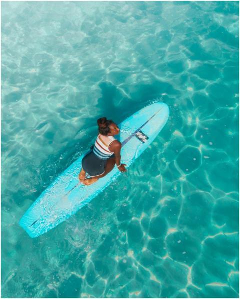 Aerial shot of a woman on a surfboard in clear, tu