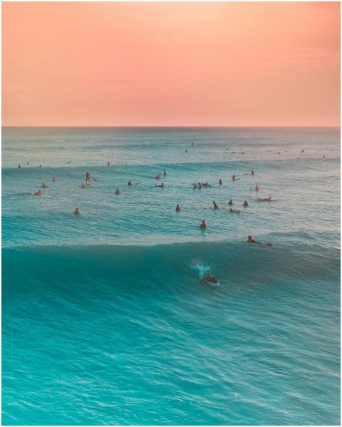 Surfers catch gentle waves under a vibrant sunset