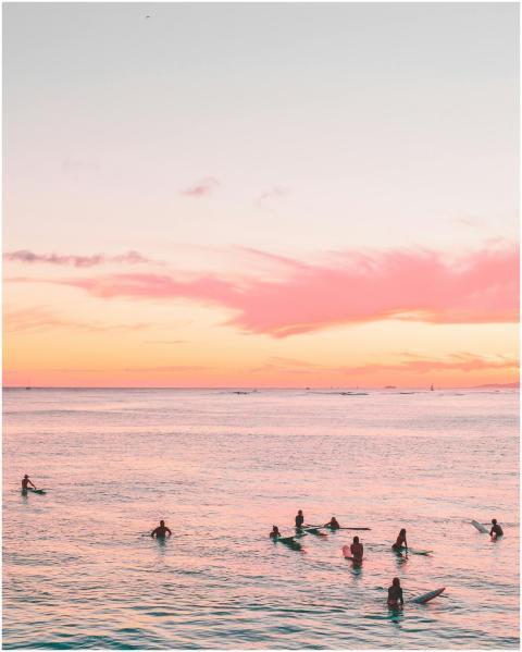 Surfers enjoy a serene sunset on calm ocean waters