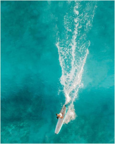 Dynamic aerial shot of a woman surfing on turquois