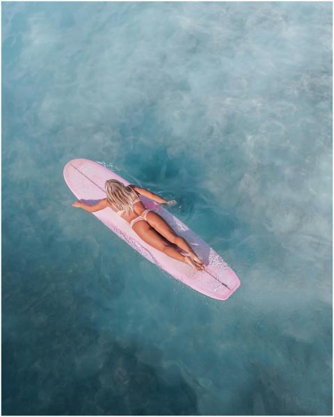 Overhead shot of a woman surfing on a pink surfboa