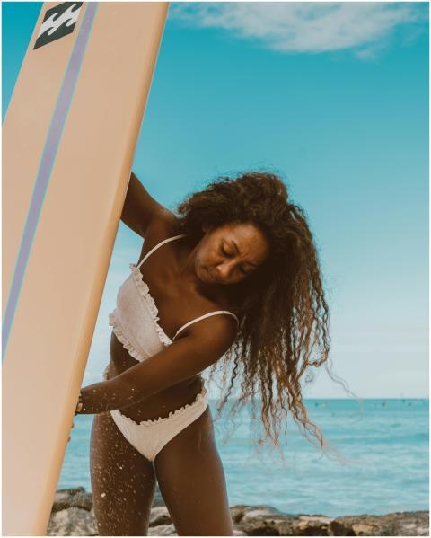 A woman in swimwear cleans her surfboard on a sunn